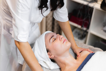 Obraz na płótnie Canvas Beautician in a spa beauty salon applies cream to a client's face, a girl lies on a cosmetology table