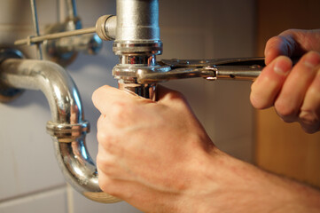 Obraz premium Young plumber is fixing a pipe with a wrench in the bath.
