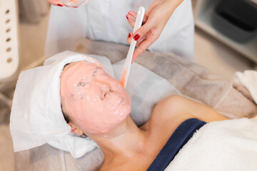 Obraz na płótnie Canvas Cosmetologist applies alginate mask with spatula on face of woman. Facial skin and anti-aging treatment. Cosmetology and professional facial skin care..