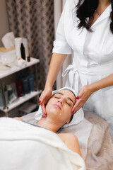 Woman client in salon receiving manual facial massage from beautician