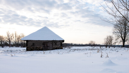 at sunset stands a snow - covered white barn made of wood in the Latvian countryside