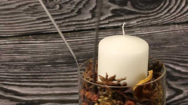 A candle in a glass candlestick with pine cones, dried fruits and sparklers. Rotates against the background of black pine boards. Close-up shot.