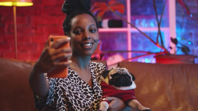 Beautiful african woman taking selfie with dog on sofa at home