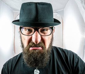 A bearded and angry looking man with black glasses and hat