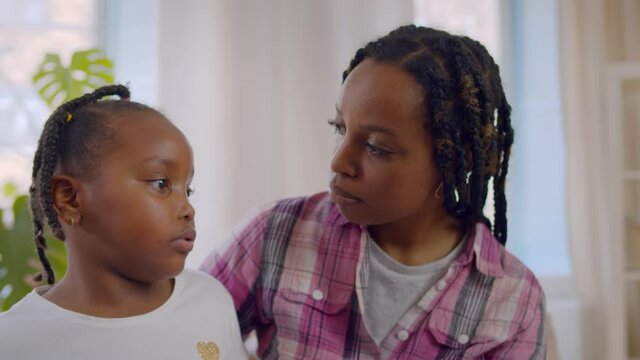 Worried afro-american mother checking little daughter body temperature kissing forehead