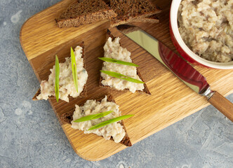 Top view of three toasts with forshmak and green onions on a wooden board. Herring forshmak in ramekin old knife on a wooden board