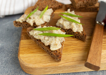 Forshmak on rye bread toast on a wooden board with a knife and green onions