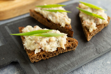 Three toasts with herring forshmak on a tapas board. Forshmak on rye bread canape with green onions