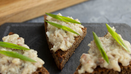 Salted herring forshmak on rye bread toast with green onions on tapas board