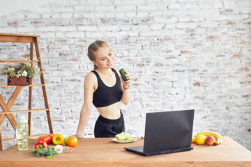 Beautiful young woman wearing sportive clothing using laptop, looking for simple recipes at home.