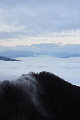 Low clouds, view of winter forest and mountains from observation deck, vertical picture of amazing natural phenomenon. Beautiful unreal panoramic view of mountains in clouds.