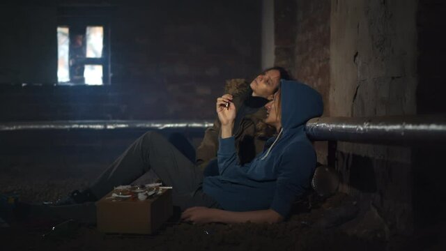 Drug addicted man and woman smoking sitting on floor in dirty basement
