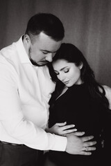 Pregnancy photo session in a photo studio with a fabric background in a black bodysuit and tights
