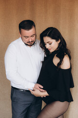 Pregnancy photo session in a photo studio with a fabric background in a black bodysuit and tights
