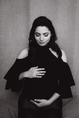 Fototapeta premium Pregnancy photo session in a photo studio with a fabric background in a black bodysuit and tights 