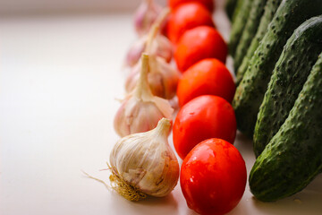 Several green cucumbers and red tomatoes and garlic  are stay in a rows on a white background