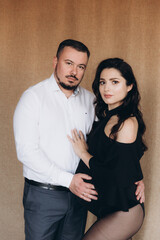 Pregnancy photo session in a photo studio with a fabric background in a black bodysuit and tights
