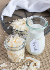 Closeup view of a tagged coconut milk in a bottle and a glass full of coconut slices. Vertical view.