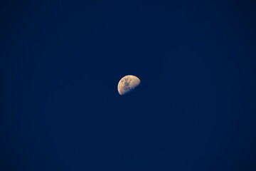 distant crescent moon, with colored surface, isolated on a dark blue twilight sky.