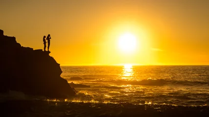 Zwei Mädchen-Silhouetten auf einer Klippe mit orangefarbenem Himmel Sonnenuntergang © Ric