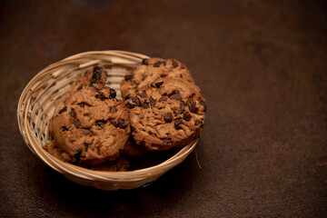 Galletas con pepitas de chocolate en una bol de mimbre sobre fondo marrón.