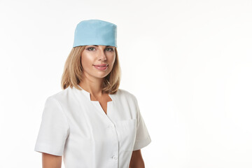Isolated portrait of a young cute doctor wearing white uniform and blue medical hat standing on white background and smiling at camera