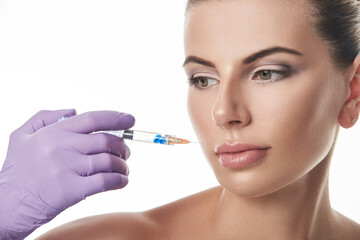 Beautician's hand in purple glove holding a syringe near beautiful woman's face. Portrait isolated on a white background. Anti-aging treatment.
