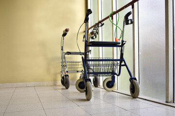 In a desolate corridor, two walking aids for elderly people are chained to a glass wall, in front...