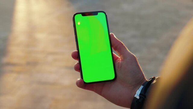 Close up man young hand using touch phone with vertical green screen background sunlight road in city blurred. Internet chrome outdoor cellular smartphone scrolling tapping. Slow motion