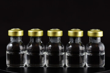 Several ampoules with transparent liquid, without a label, stand next to each other against a dark background and space for text