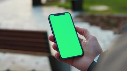 Close up young hands man holding use phone with vertical green screen in park background bench. Internet finger gadget device. Slow motion - Powered by Adobe