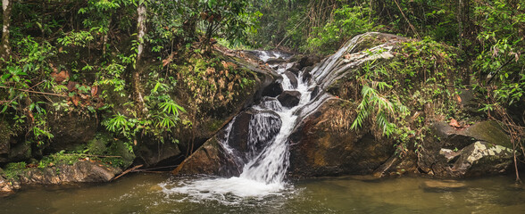 Waterfall landscape in tropical jungle of Thailand. Beautiful Thai panoramic nature scenery with falling river water on stones rocks, rainforest green trees in Khao Lak Lam Ru National Park, Thailand