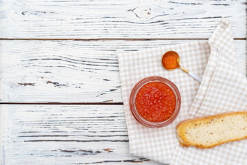 Red salmon caviar in glass jar on napkin and wooden backdrop. Text space. Tasty snack.