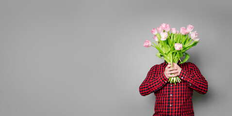 Young man in checkered shirt with pink tulips on gray backdrop. Woman's day, 14 february, Mother's day concept. Text space. Banner