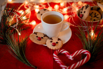 Christmas card, decor, cup of tea, ginger New Year's deer, sweets in the shape of a heart, lights, tree on a red background. view from above
