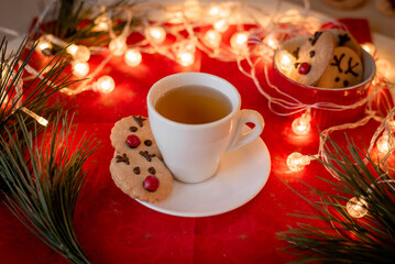 Christmas card, decor, cup of tea, gingerbread New Year's deer, candies, lights, tree on a red background