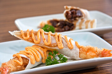 Shrimp tacos with burrito style chipotle chili dressing on white square plate over wood background, close up view