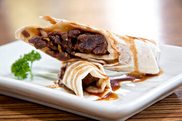 Rib eye tacos with burrito style tamarind sauce on a square white plate over wood background, close up view