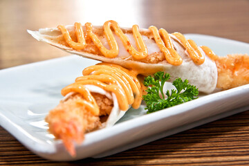 Shrimp tacos with burrito style chipotle chili dressing on white square plate over wood background, close up view