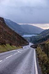a winding road down the mountain pass leading to the lake at the bottom