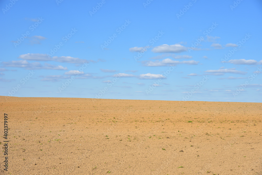 Wall mural view of a deserted sand field against a blue sky with clouds.