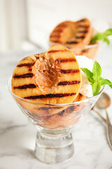 Delicious grilled peach with ice cream and mint on white marble table