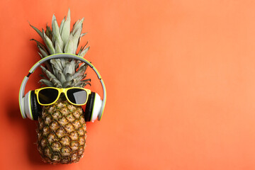 Top view of pineapple with headphones and sunglasses on orange background, space for text. Creative...
