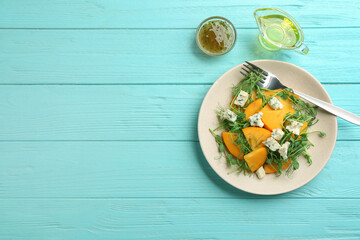 Fototapeta na wymiar Delicious persimmon salad with blue cheese on light blue wooden table, flat lay. Space for text