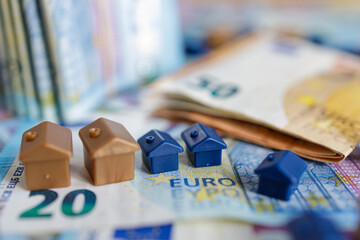 House models on background of European twenty and fifty euro bills banknotes surrounded by coins.