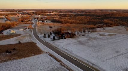   Aerial view of American Midwestern countryside landscape in spring winter season. Agricultural fields covered in snow, farm houses. Sunny, sunset 