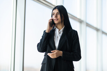 Businesswoman standing against office window talking on mobile phone