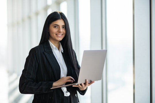Young business woman with laptop standing in an office windows