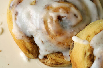 Two Sweet Rolls  with white frosting flowing down the sides, photographed from directly above.  One roll is leaning against the other.
