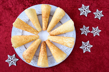 Norwegian Krumkake cookies on a white snowflake platter on a rich red background
